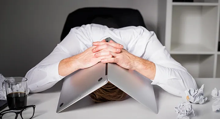 Businessman stressed with head underneath a laptop
